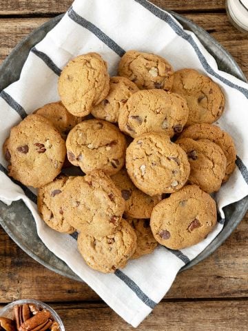 Top view of pile of chocolate chip cookies on a striped cloth set on a wooden surface.