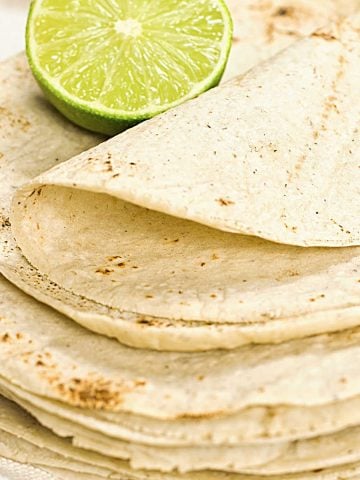 Close up of homemade corn tortillas stack with half a lime on top.