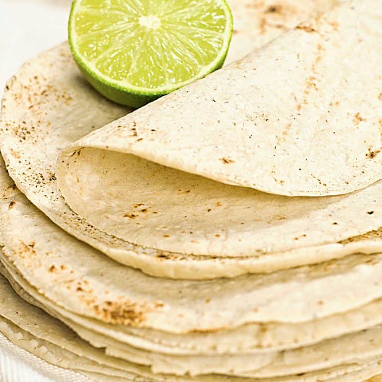 Close up of homemade corn tortillas stack with half a lime on top.