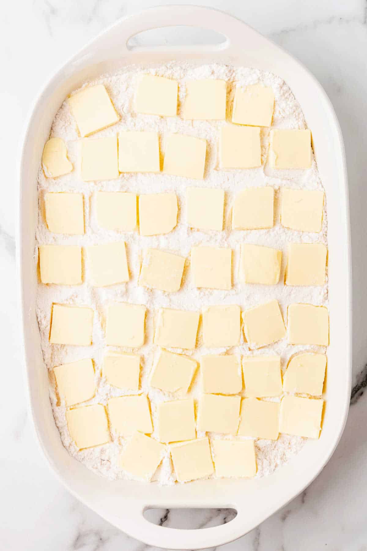 Butter slices on cake mix in a white rectangular dish on a white marble surface.