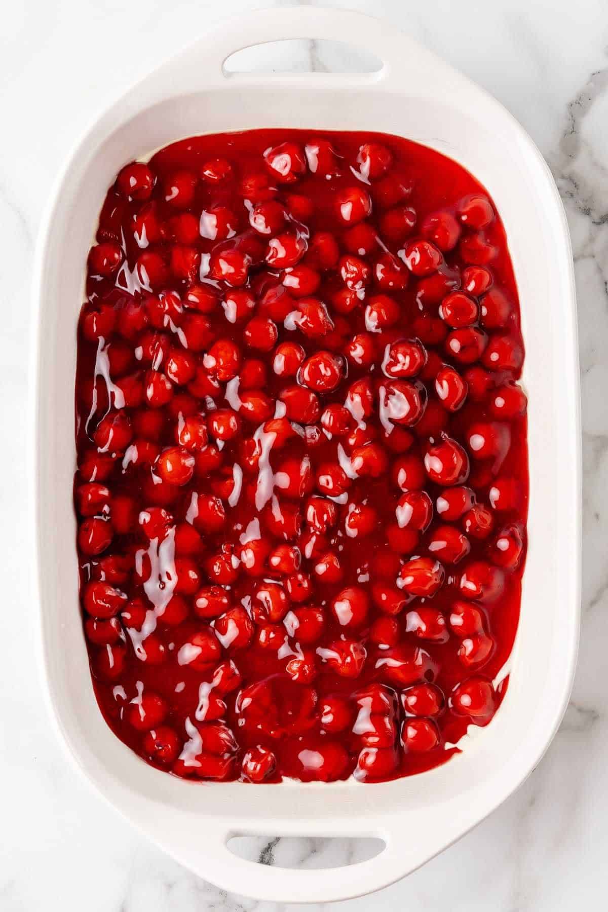 Cherry pie filling in a white rectangular dish on a white marble surface.