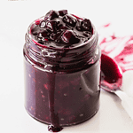 Jar of blueberry sauce with white and pink text overlay.