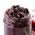 Brown and purple text overlay on jar of blueberry sauce.