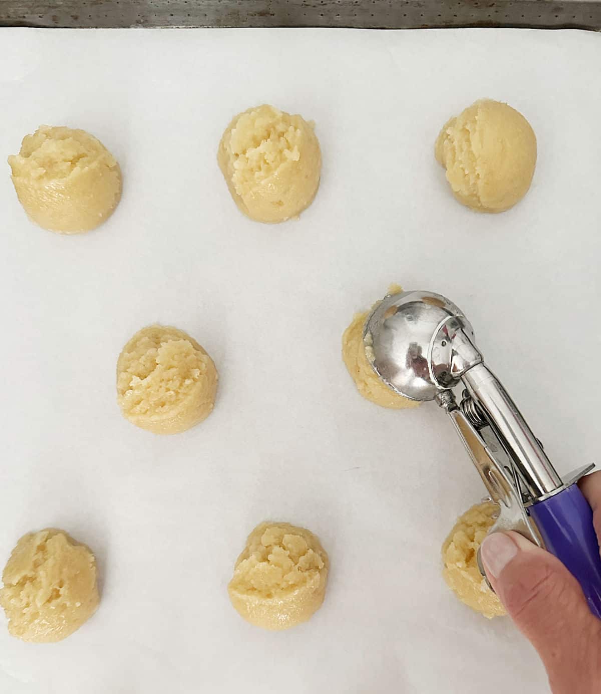 Scooping vanilla cookie dough on white parchment paper. 