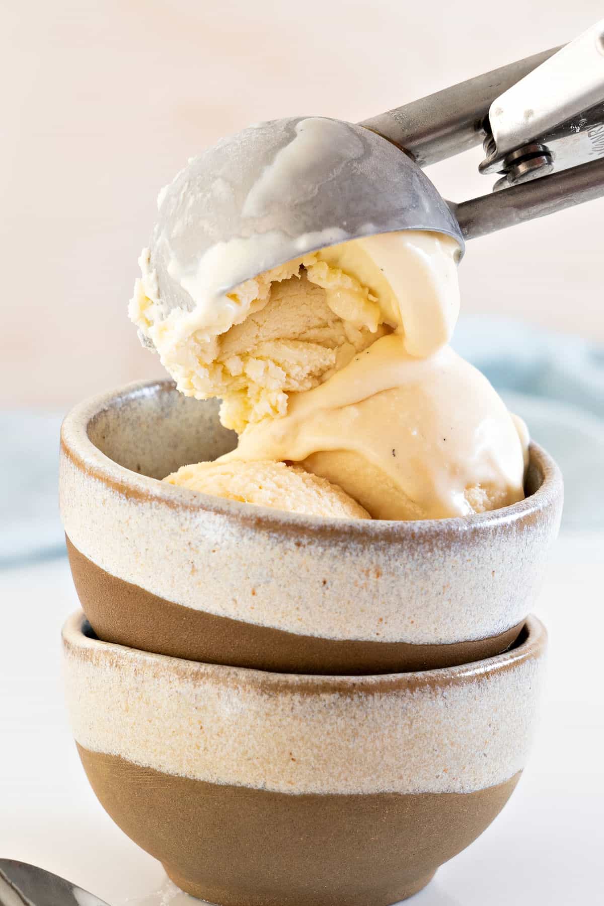 Two stacked bowls with vanilla ice cream being scooped. Pinkish background.