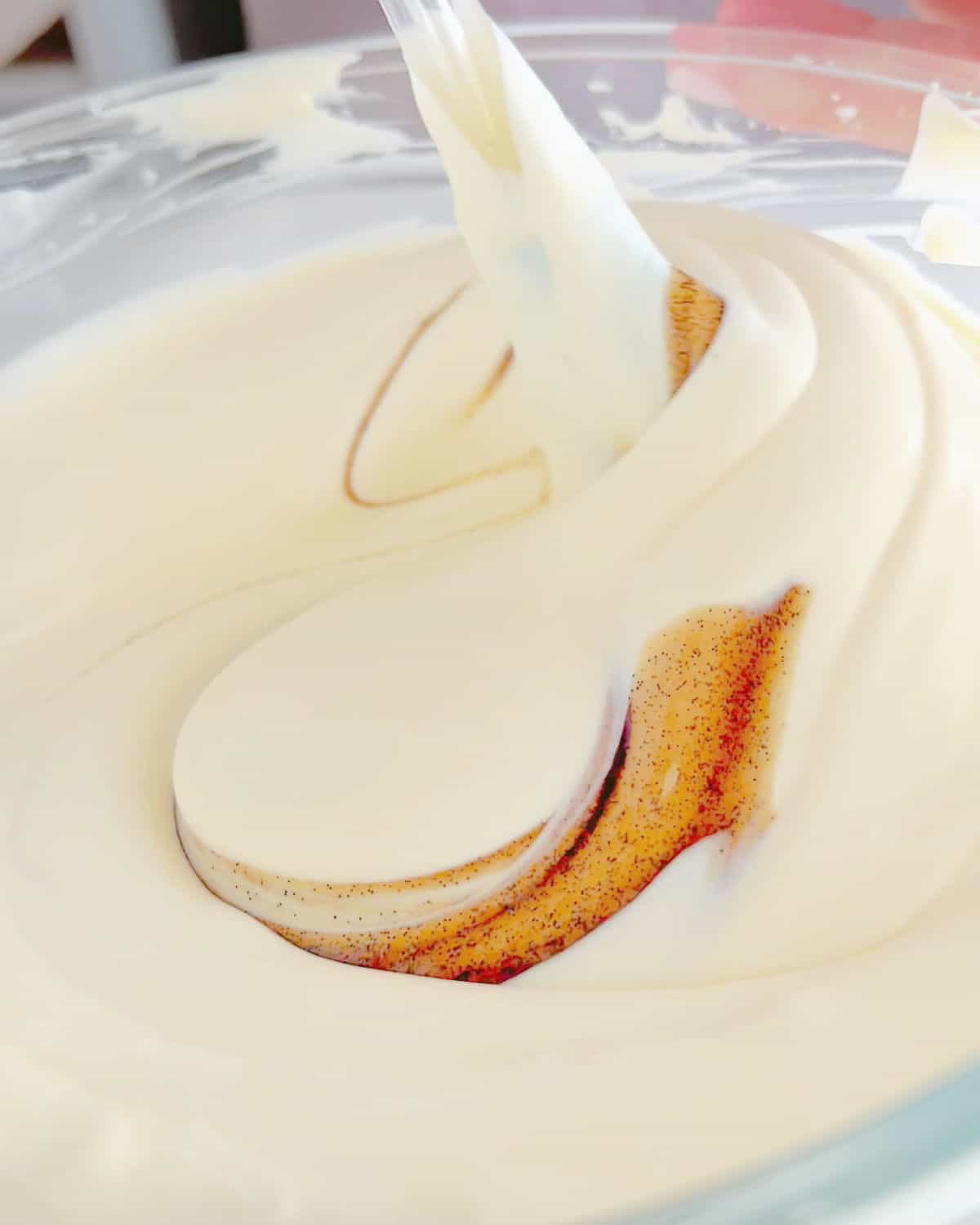 Folding in vanilla paste into whipped cream in a glass bowl with a spatula.