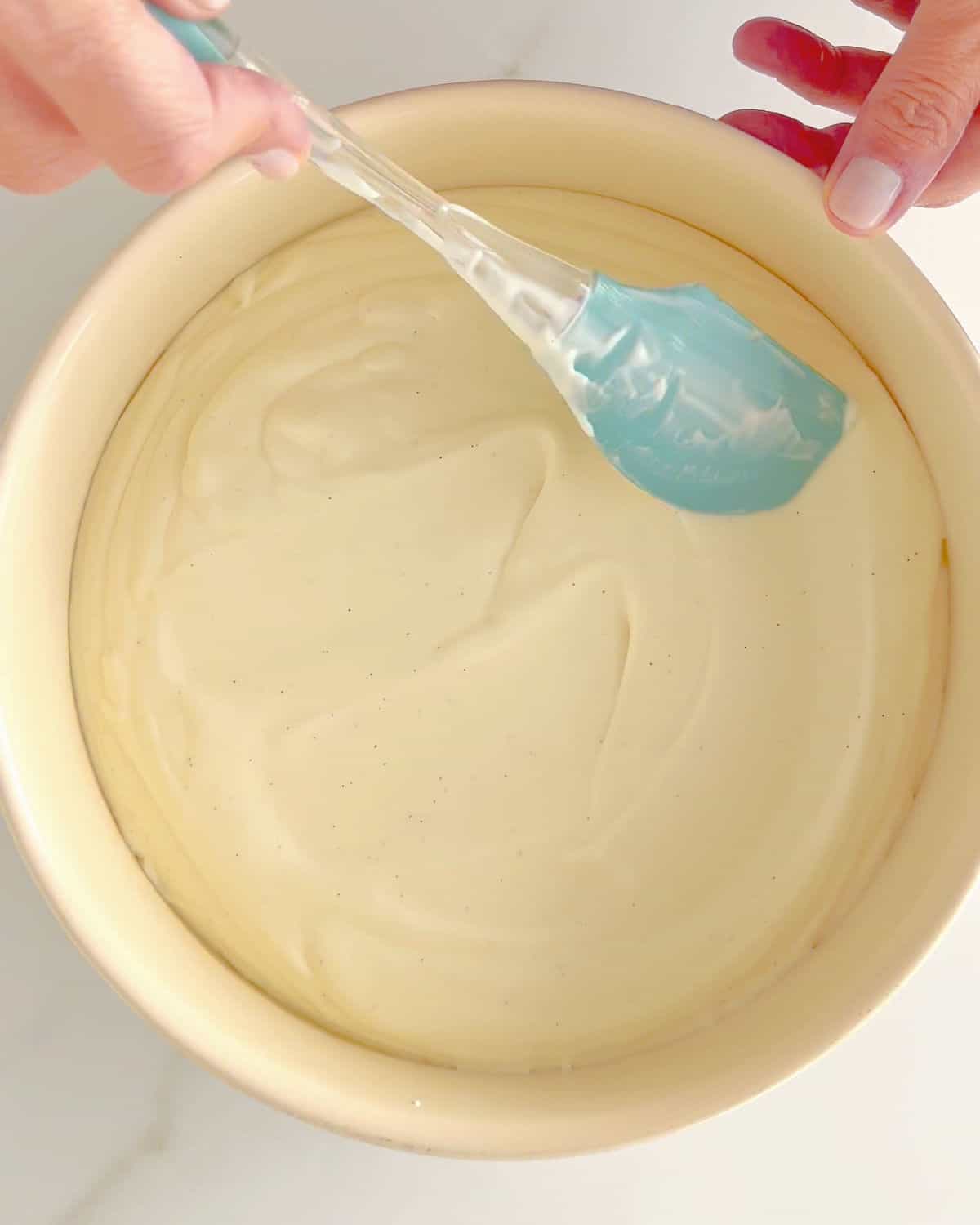 Vanilla ice cream being evened out in a round metal beige pan with a blue spatula.