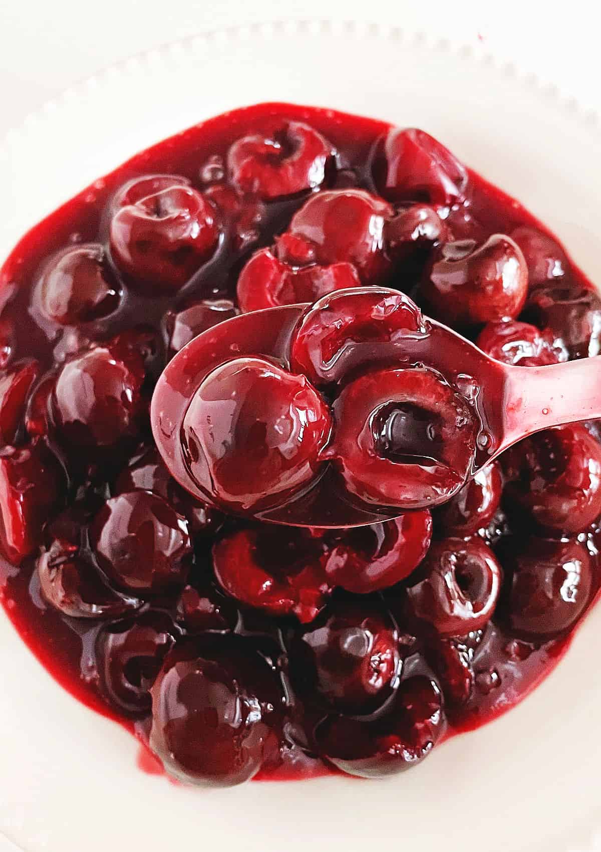Spooning cherry sauce over white bowl with cherry topping.