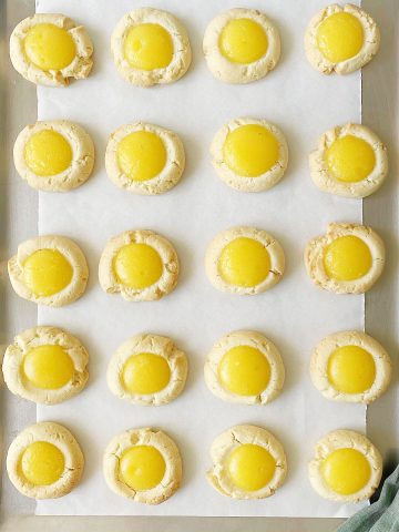 Batch of baked lemon curd cookies on a cookie sheet with white parchment paper.