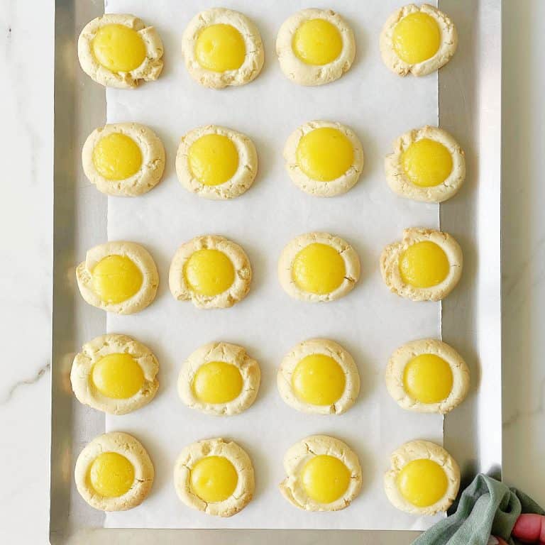 Batch of baked lemon curd cookies on a cookie sheet with white parchment paper.