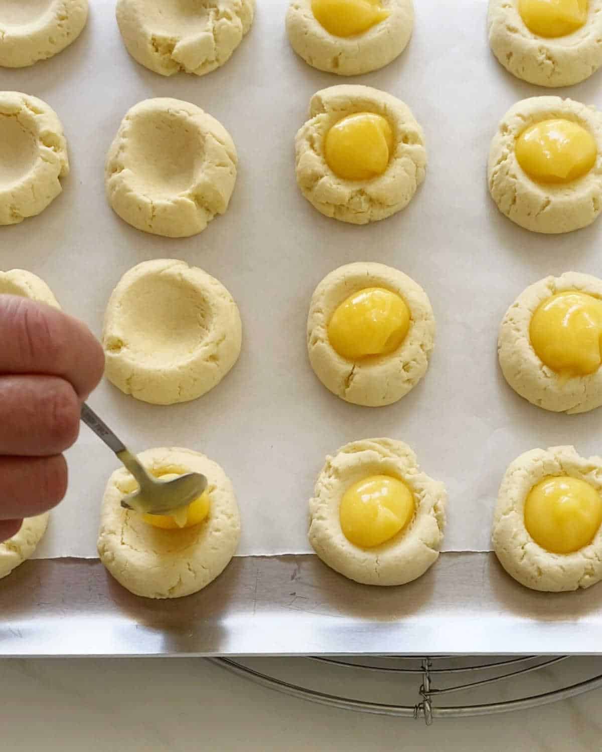 Filling thumbprint cookies on a parchment-lined baking sheet with lemon curd.