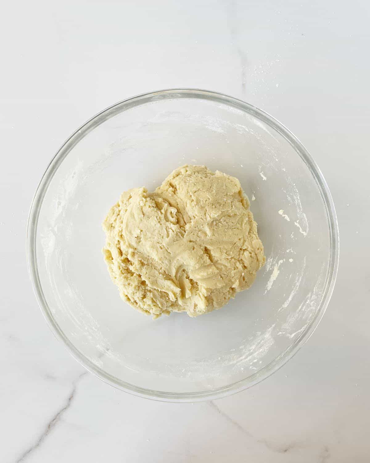 Cookie dough for thumbprints in a glass bowl on a white marble surface.