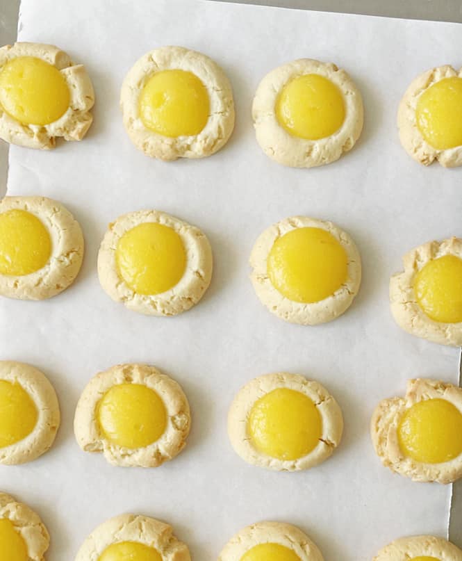 Top view of baked lemon curd thumbprint cookies on white parchment paper.