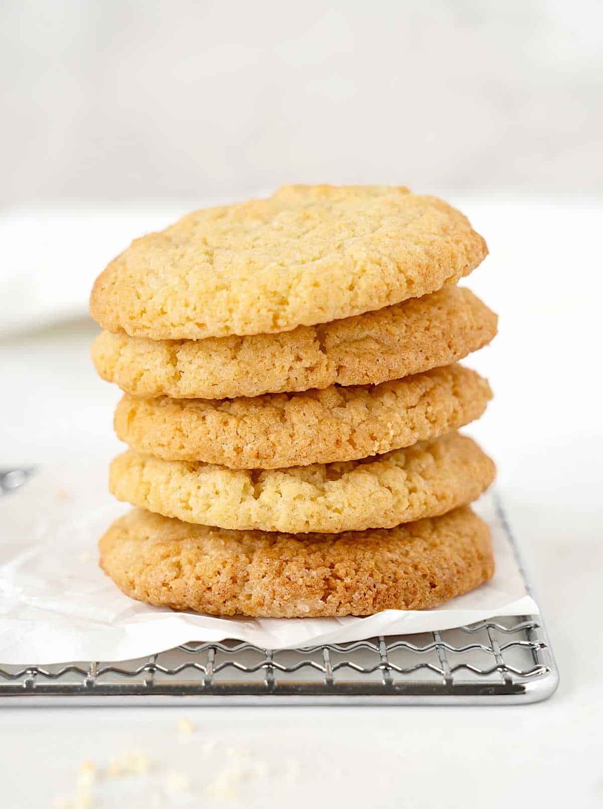 Vanilla cookies in a stack on white parchment paper on a wire rack. White surface and background.