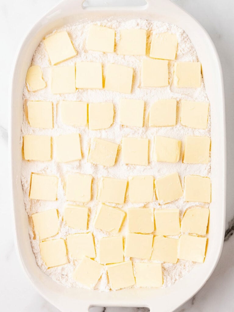 Butter slices on top of cake mix in a white rectangular baking dish.