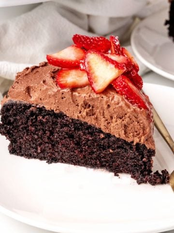 Mousse topped slice of chocolate cake with strawberries on a white plate with a fork.