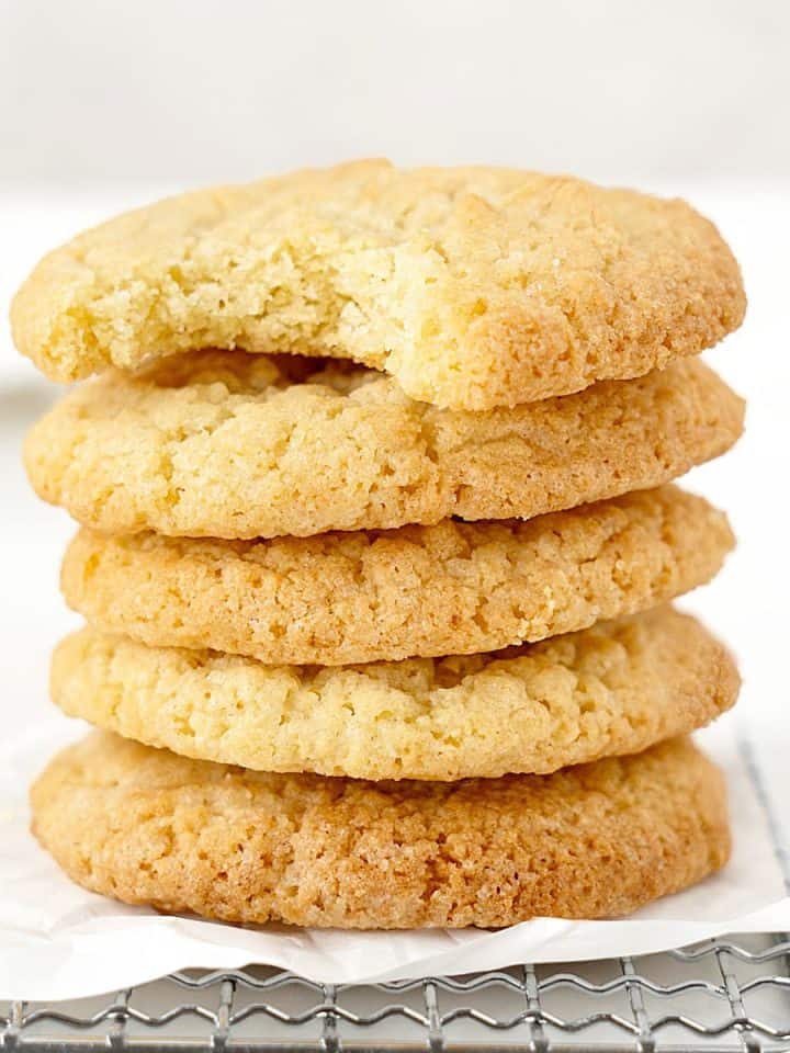 Top cookie bitten of stack of vanilla cookies on white paper and white background.