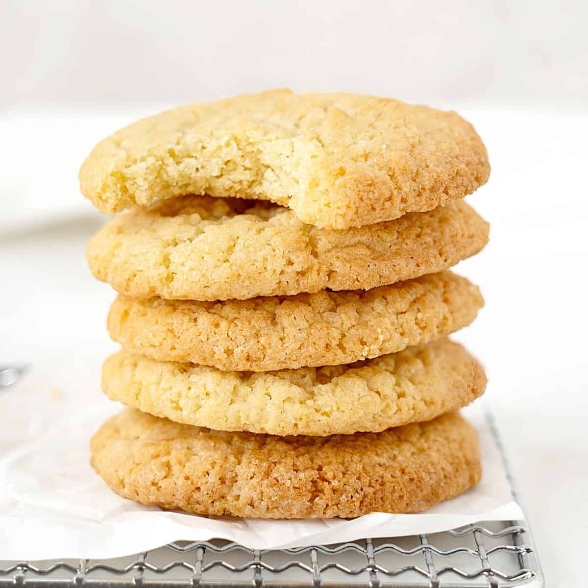 Top cookie bitten of stack of vanilla cookies on white paper and white background. 