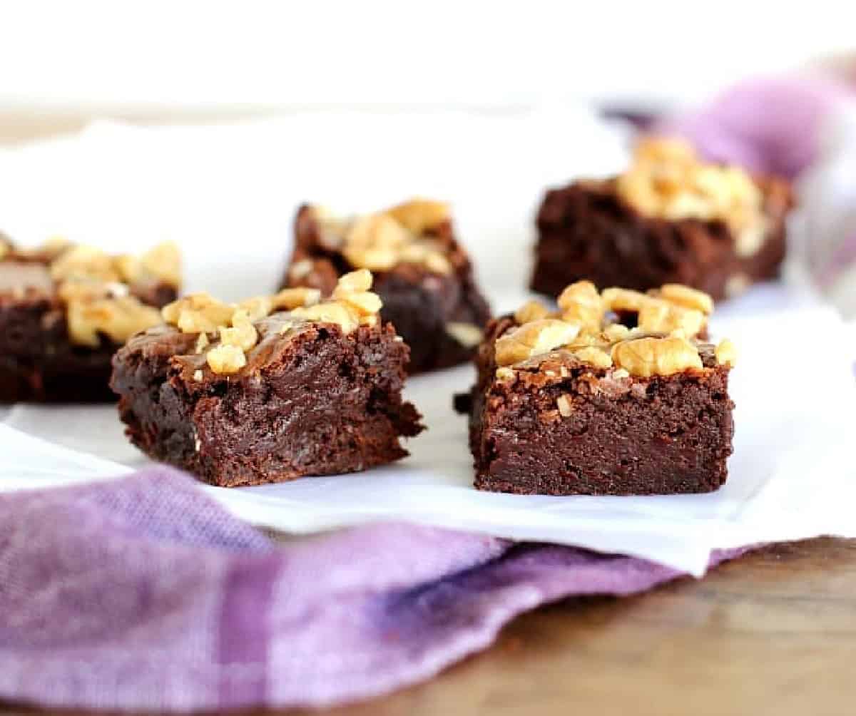 Several walnut brownies on parchment paper on a purple towel.
