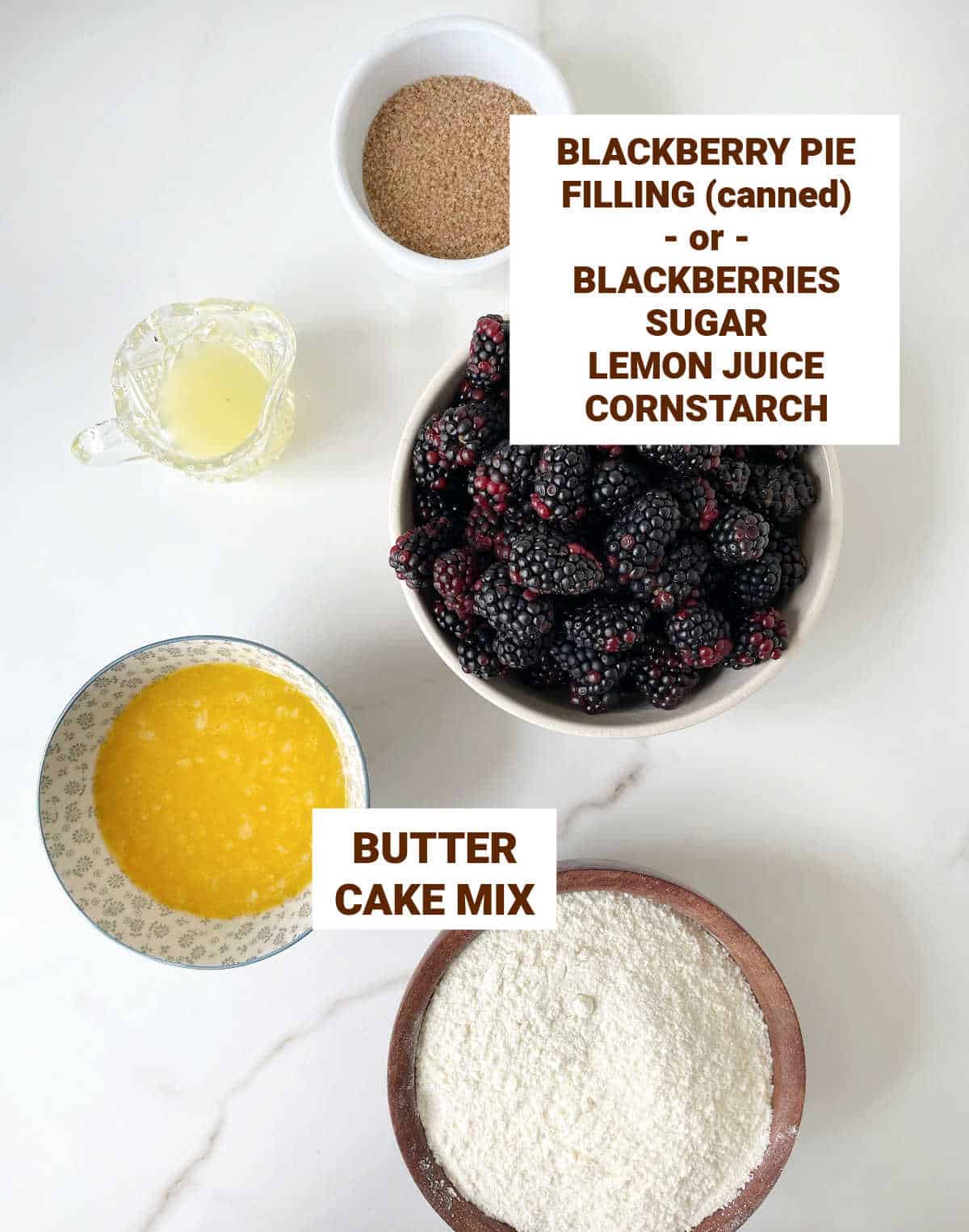 White marble surface with bowls containing ingredients for blackberry dump cake including butter, sugar, lemon juice, and cake mix.