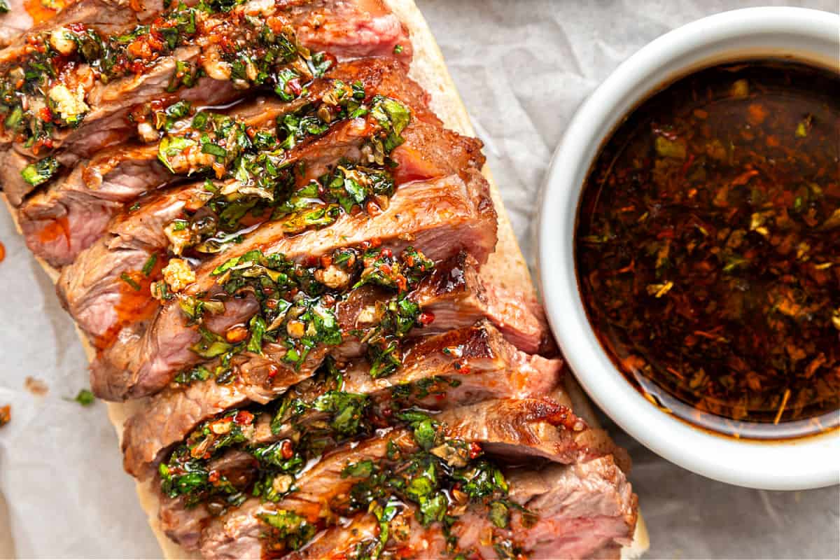 Marinated Steak and Chimichurri Sliders Chimichurri drizzled steak slices on white bread. Bowl with sauce.