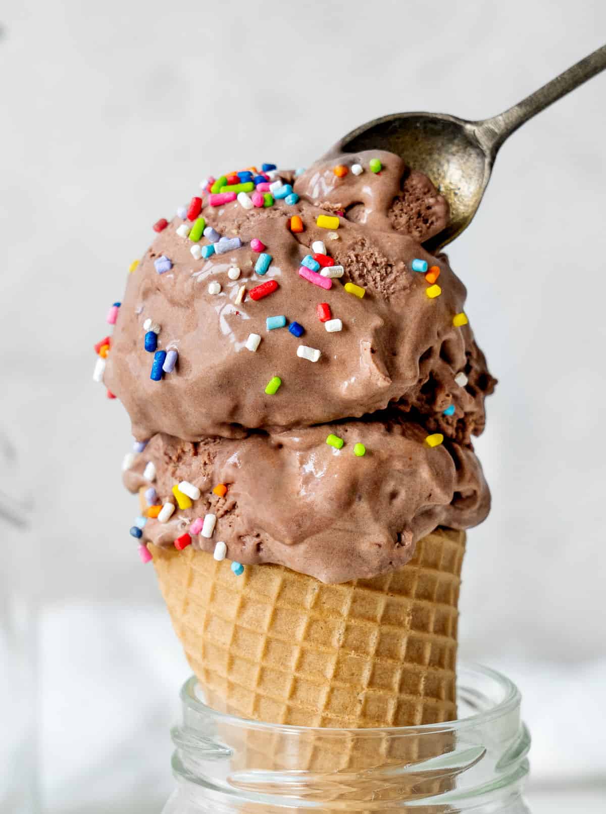 Spooning chocolate ice cream with sprinkles in a waffle cone. Light grey background. 