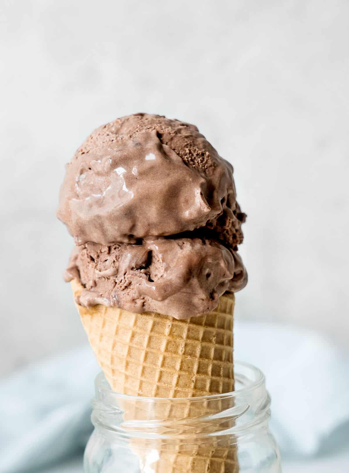 Waffle cone with two scoops of chocolate ice cream. Light grey and light blue background. 