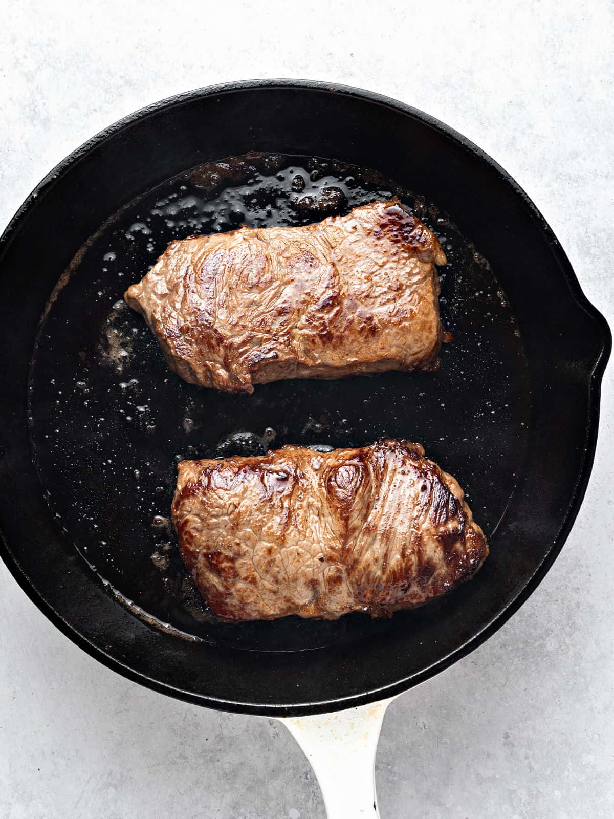 Cooking two steaks in a black skillet.