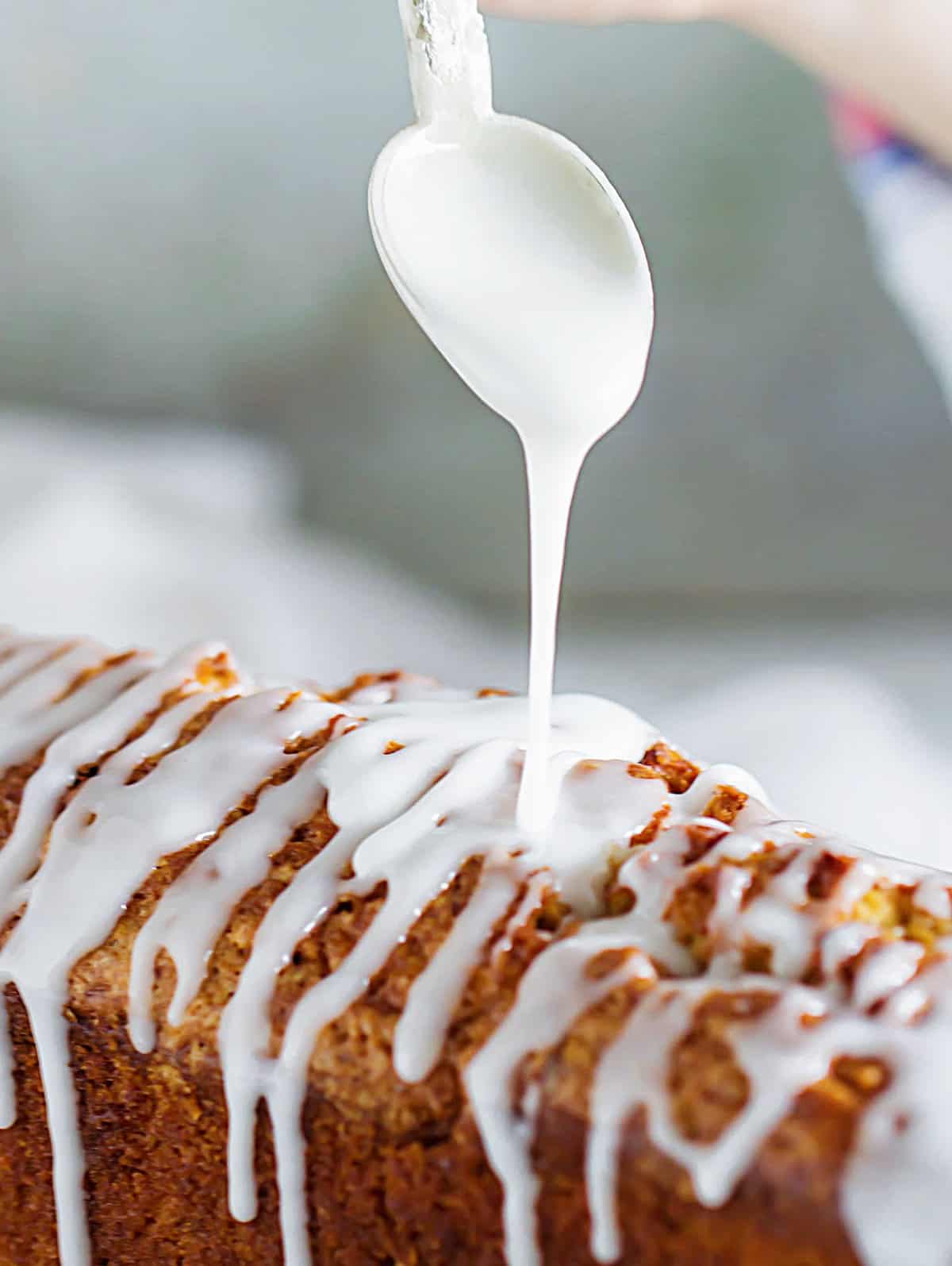 Loaf cake being drizzled with powdered sugar glaze from a silver spoon. 