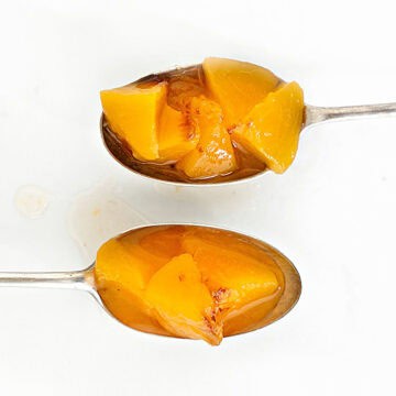 Two silver spoons with peach compote on a white surface.
