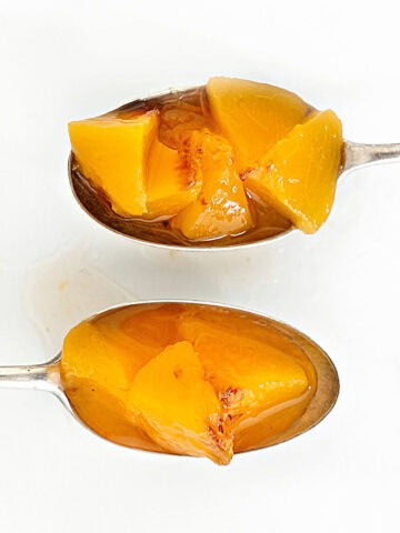 Two silver spoons with peach compote on a white surface.