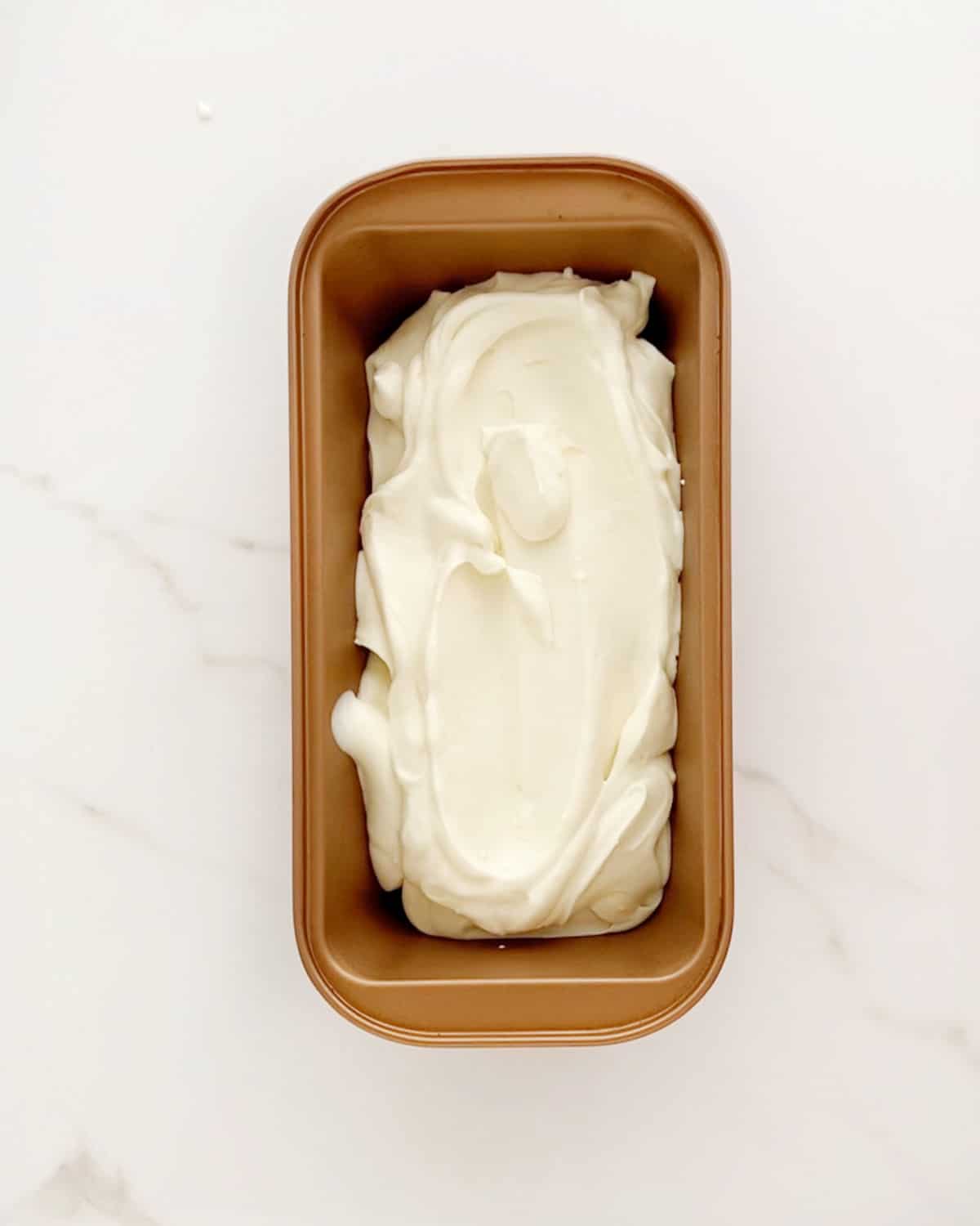 Lemon ice cream in a copper loaf pan on a white marble surface.