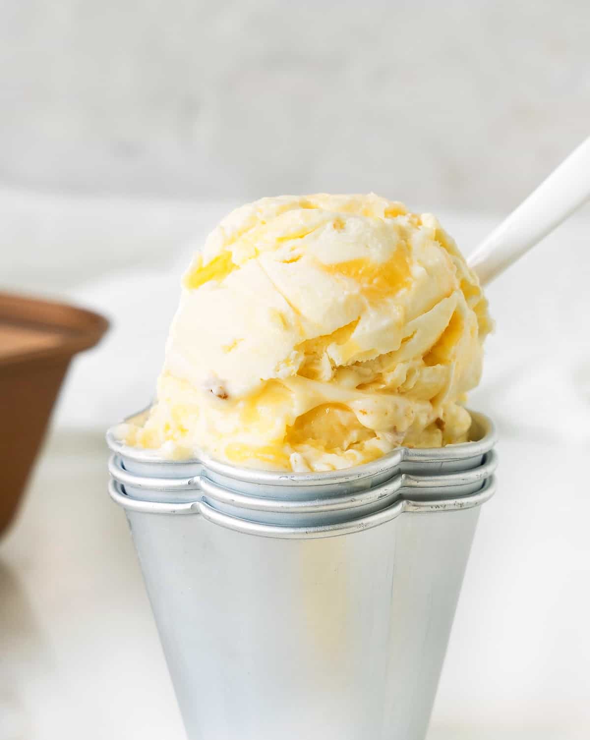 Metal cup with scoop of lemon curd ice cream. White surface and background.