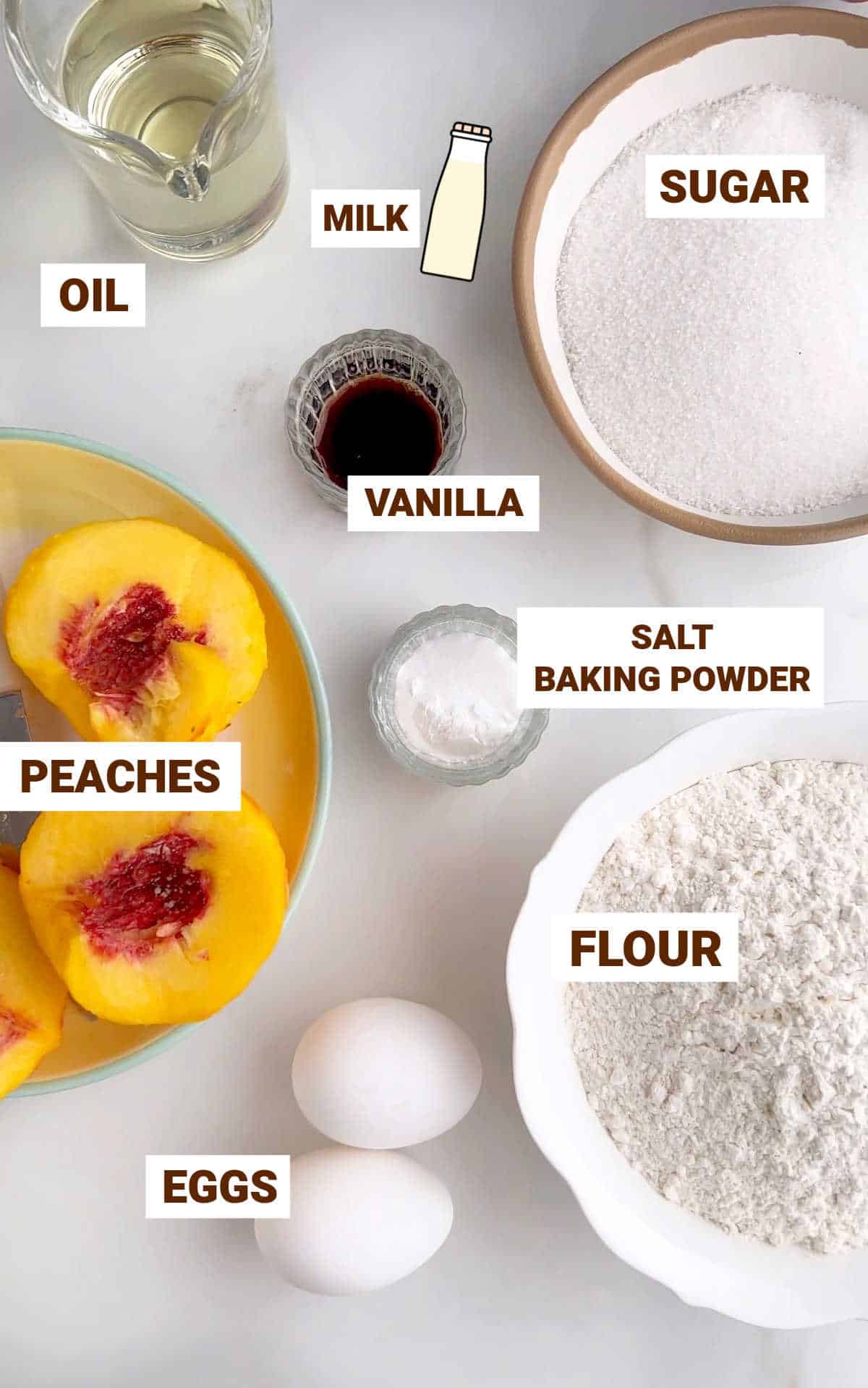 White marble surface with ingredients for peach muffins including eggs, oil, sugar, vanilla, flour mixture.