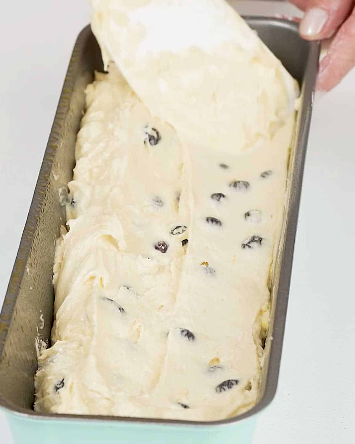 Smoothing blueberry cake batter in a loaf pan with a white spatula.