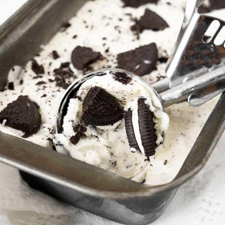Metal loaf pan with Oreo ice cream and a silver ice cream scoop.