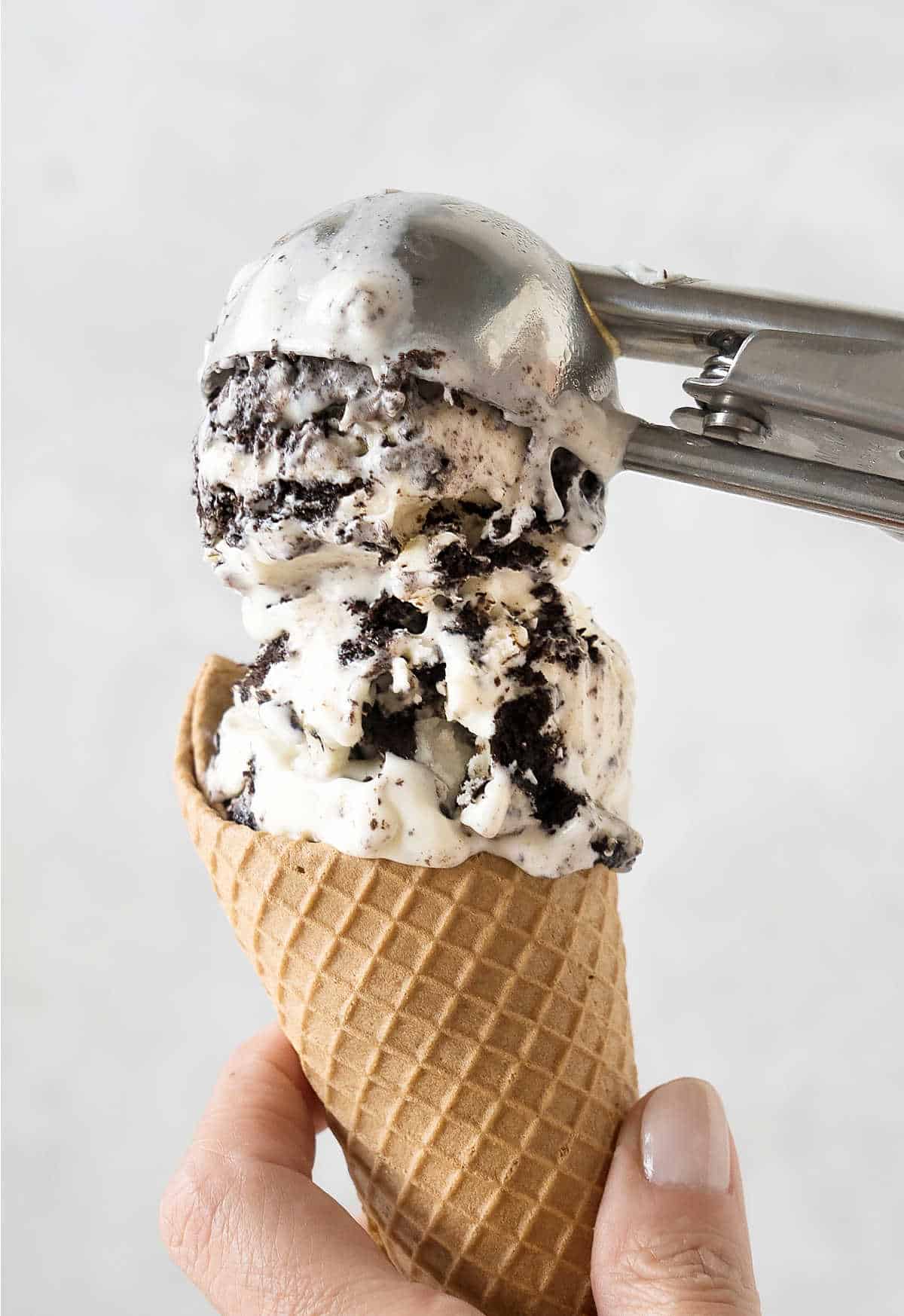 Scooping oreo ice cream in waffle cones. Light grey background. 