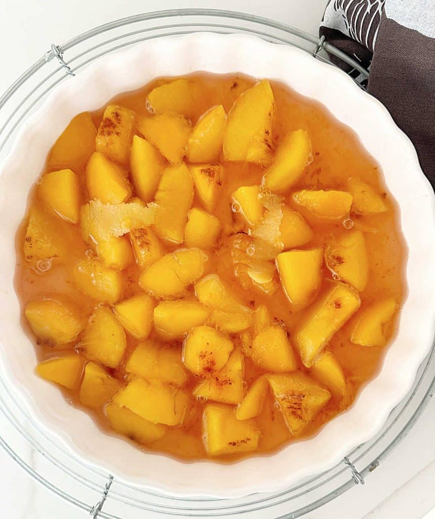Round white ceramic dish on a wire rack with peach compote. White surface.