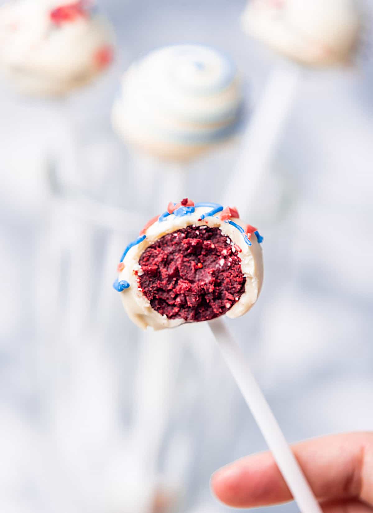 Single bitten red velvet white chocolate cake pop on a blurry bluish background.