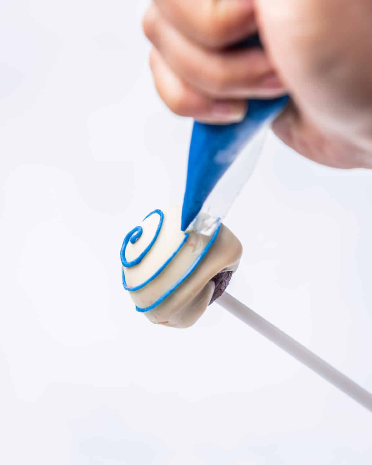 Making stripes on a white cake pop with blue icing pastry bag.