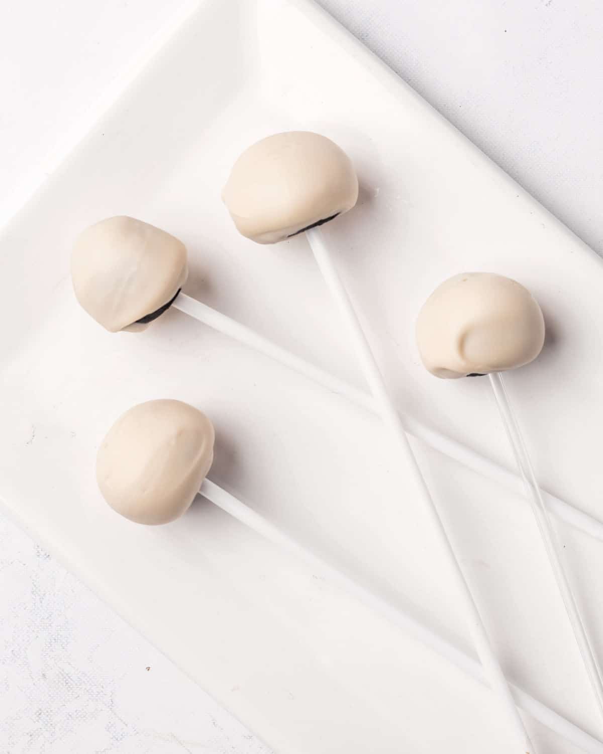 Four white chocolate covered cake pops on a white tray.