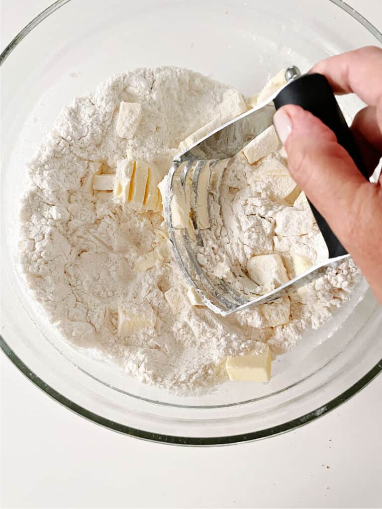 Cutting in butter into flour mixture in a glass bowl with a pastry cutter.