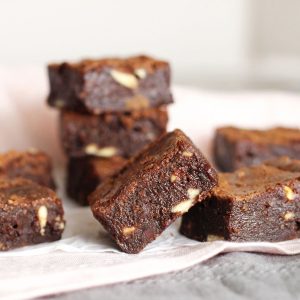 Several triple chocolate brownie squares on a pink and grey cloth. White background.