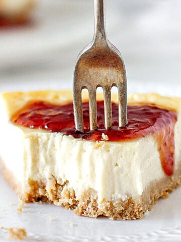 White background and plate with eaten slice of jam covered cheesecake. Silver fork.