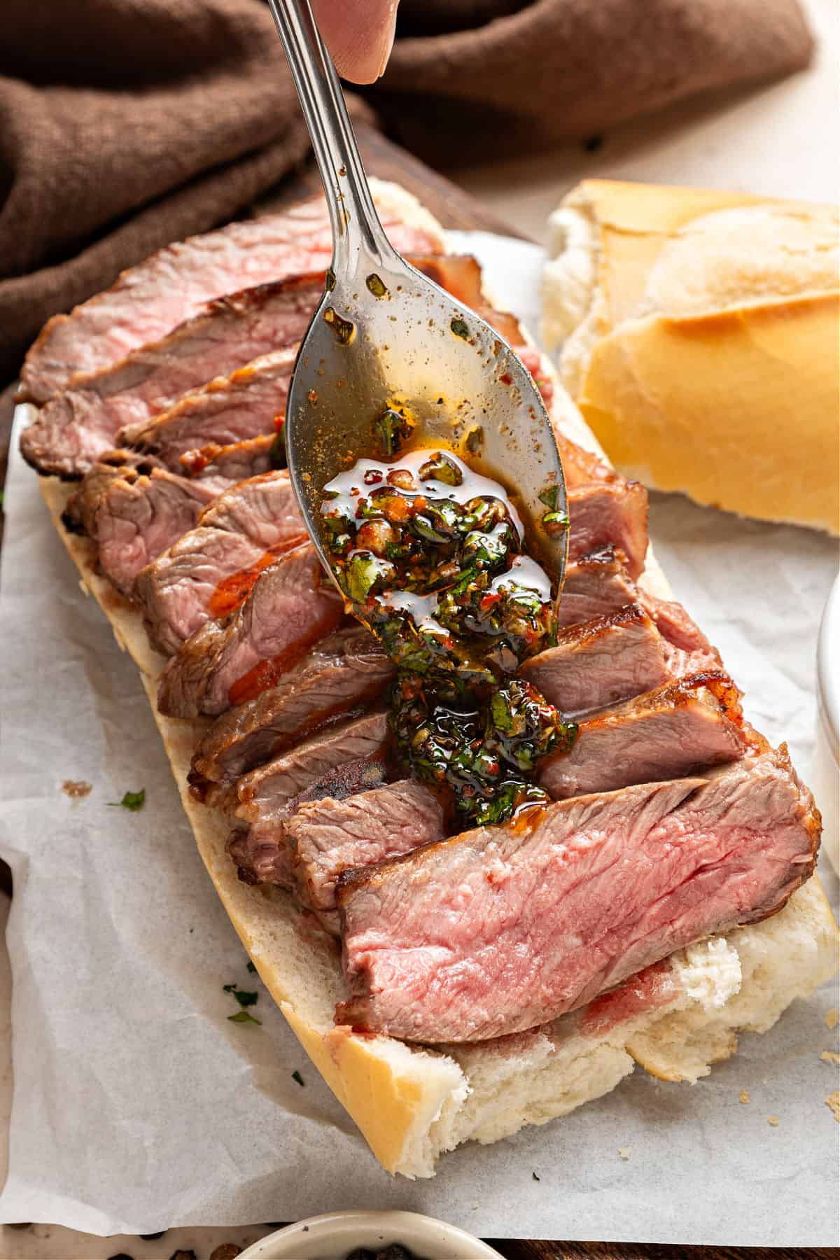 Spooning chimichurri on sliced steak on bread half.