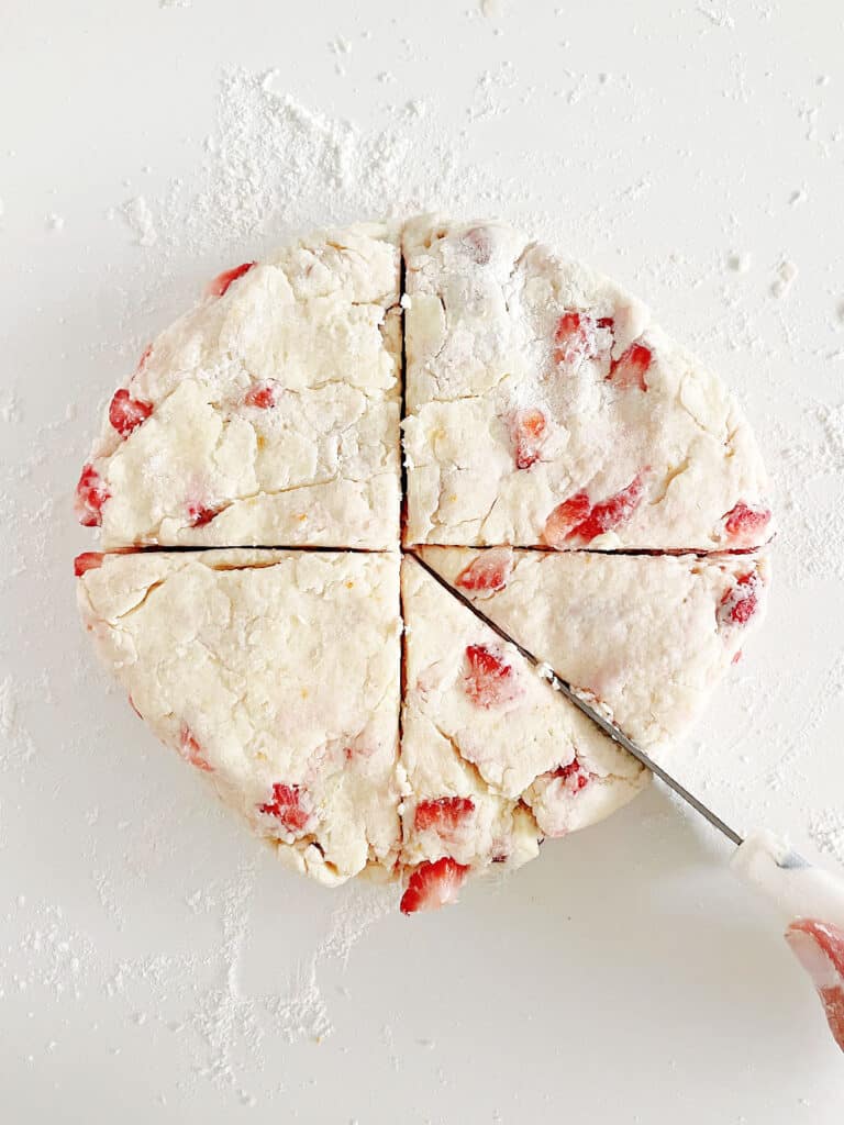 Cutting a circle of strawberry scone dough with a knife. White surface. 