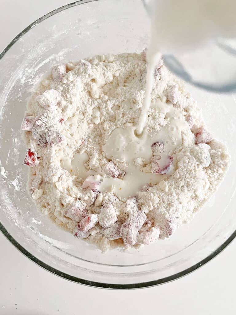 Adding milk to strawberry scone mixture in a glass bowl. 