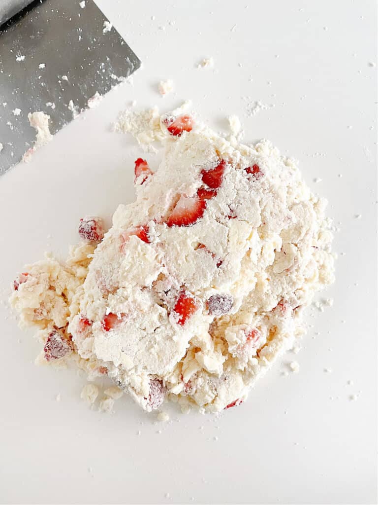 Rough strawberry scone dough on a white surface. A dough scraper. 