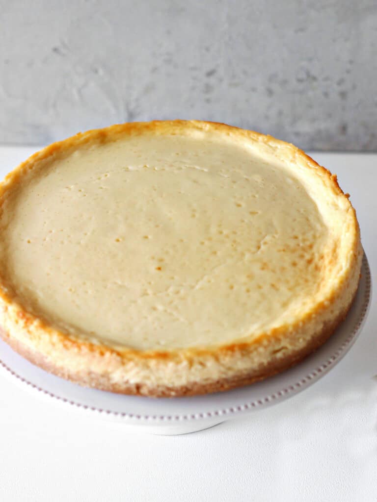 Baked sour cream cheesecake on a white plate. White and gray background.