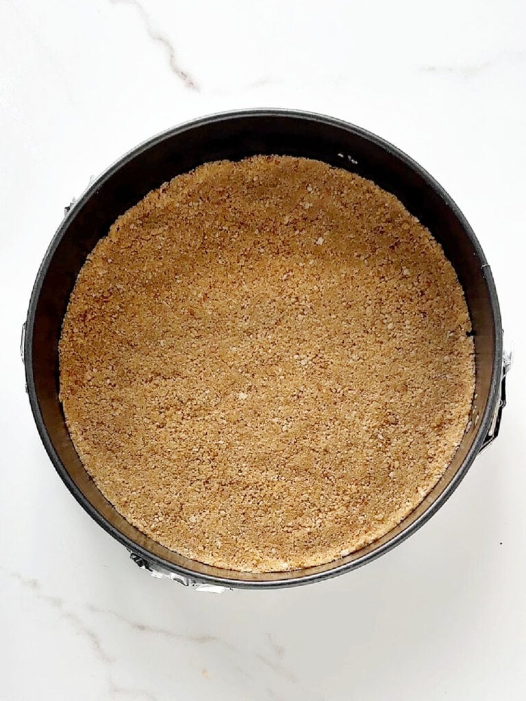 Round cake pan with graham cracker crust. White marbled background.
